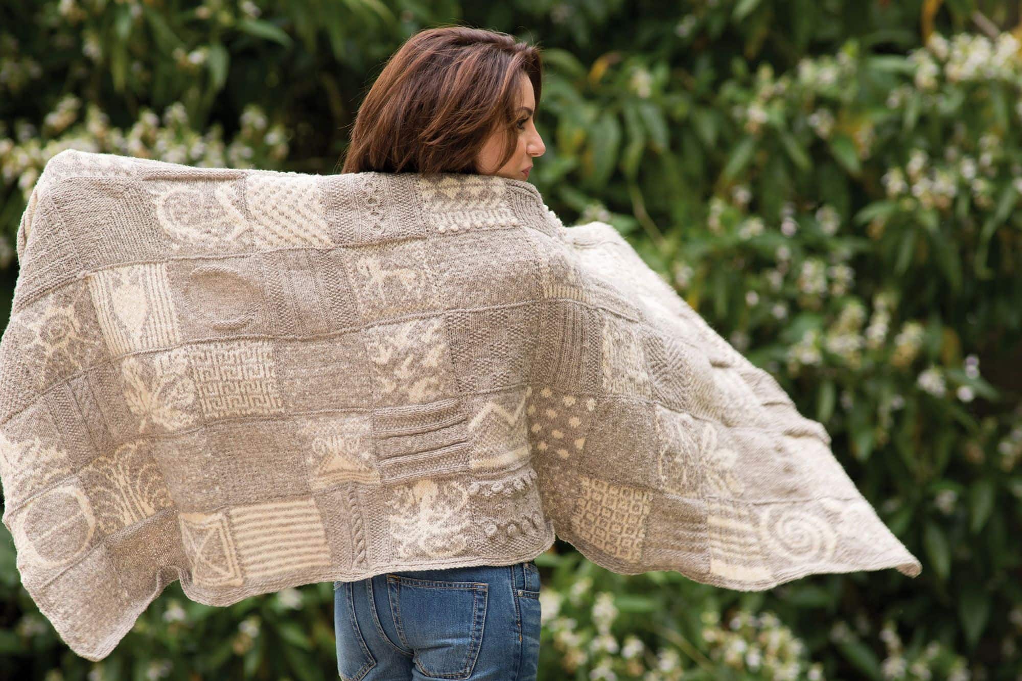 s006-9462100-ariadnes-faeden-plaid-web Frau hebt helles Wollplaid hinter ihrem Rücken als Beispiel für das Buch ,,Ariadnes Fäden"