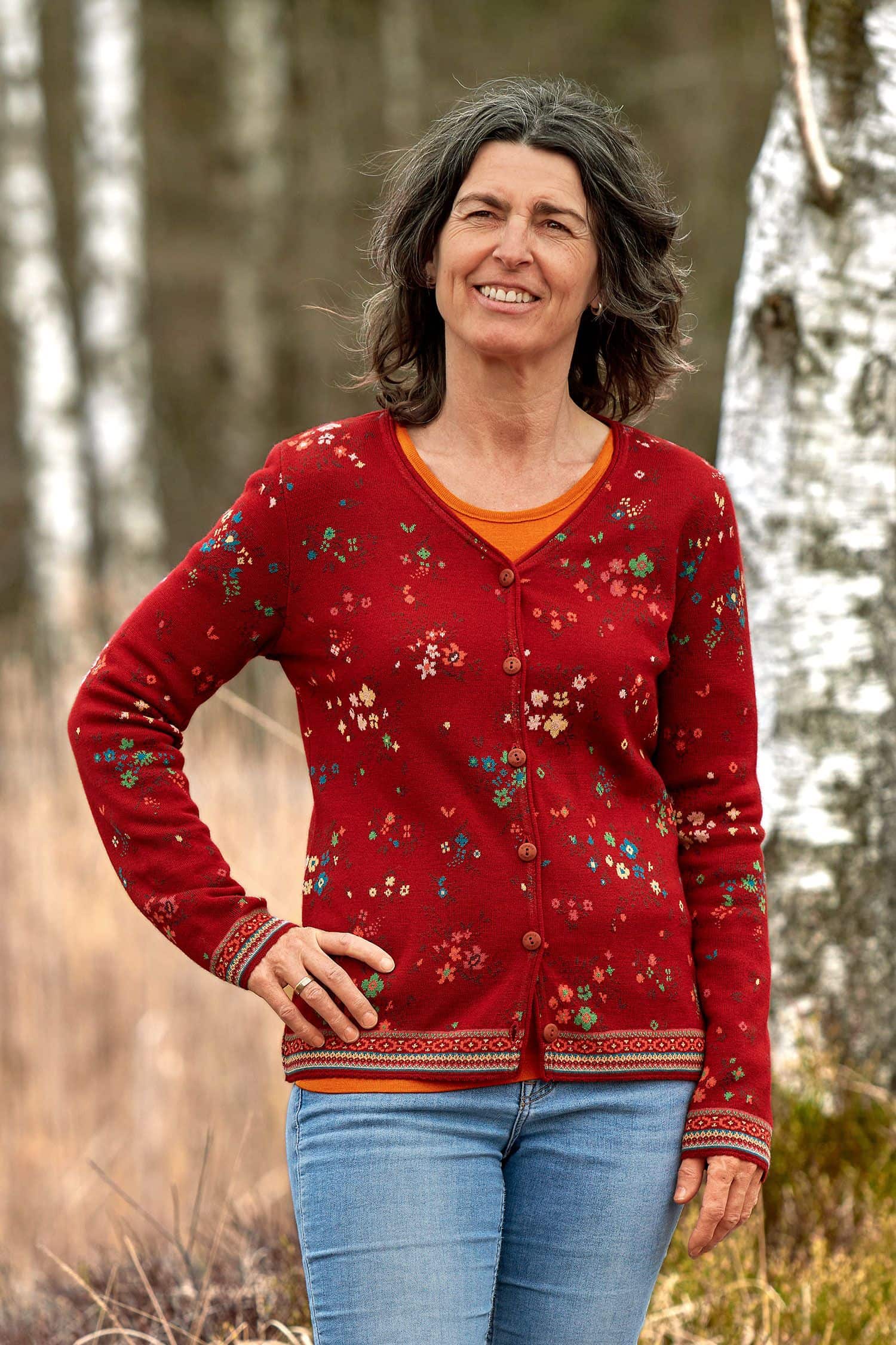 Frau mit Jeans und orangem Shirt trägt eine rot gemusterte Weste aus bio Merinowolle (kbT) und bio Baumwolle (kbA)