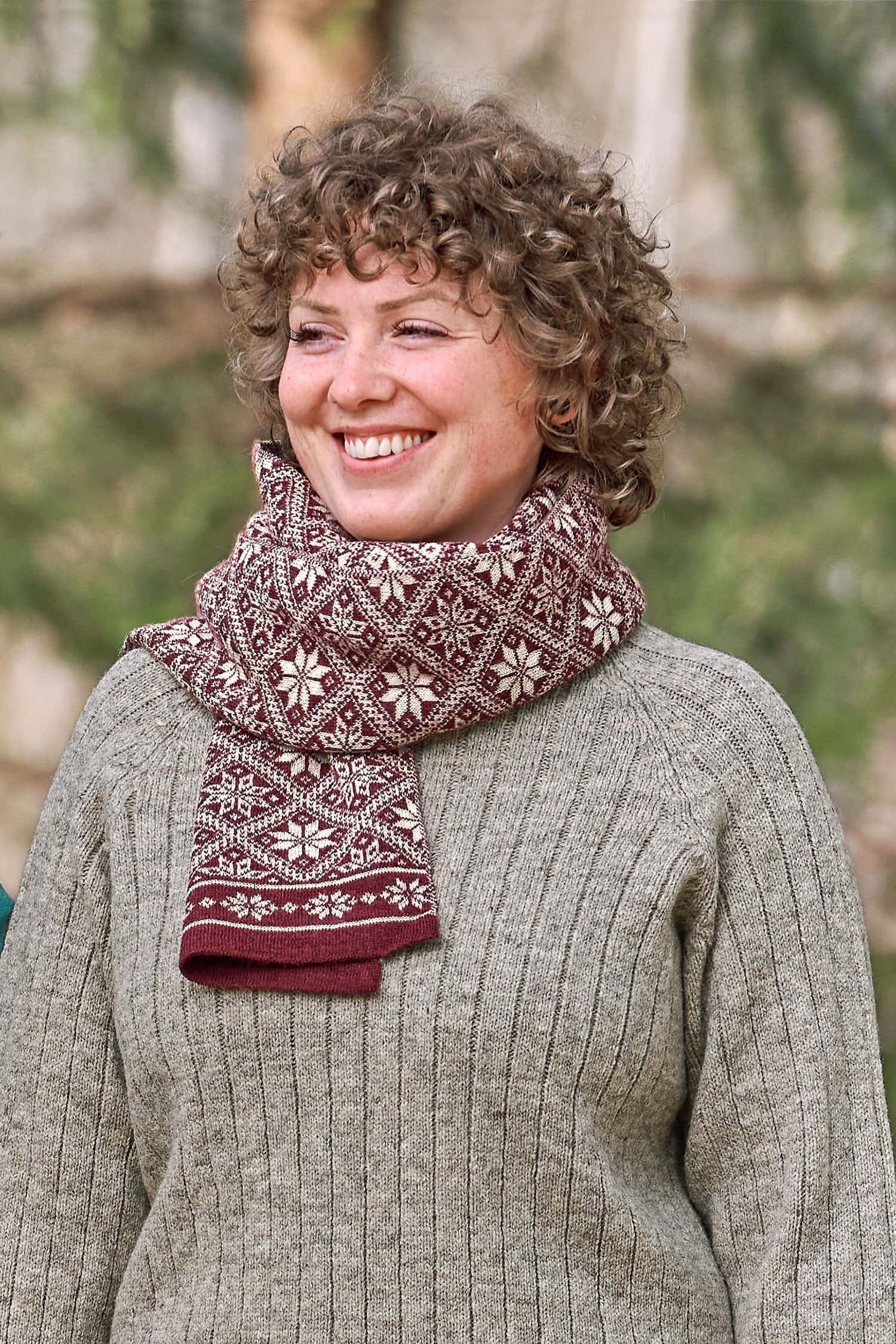 Frau mit grauem Strickpulli trägt roten Schal mit winterlichem Muster aus bio Wolle (kbT)