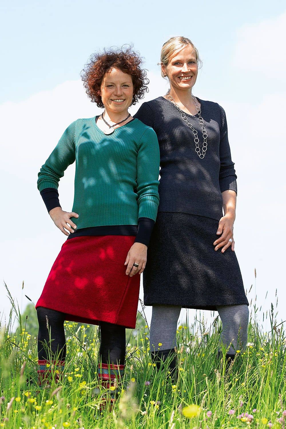 Wollkrepprock Frauen auf Wiese tragen Wollkrepprock aus bio Wolle (kbT) in anthrazit und rot mit Rippshirt, Stulpen und Accessoires