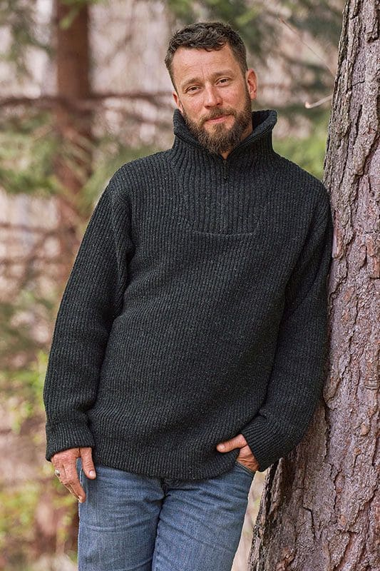 Mann mit Jeans an Baum gelehnt trägt anthraziten Finkhof Troyer mit Zipper aus bio Wolle (kbT)