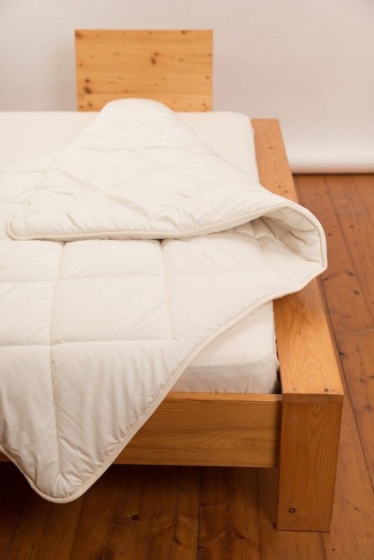 weiße Steppdecke aus bio Wolle (kbT) und bio Baumwolle (kbA) vom Finkhof auf einem braunen Bett