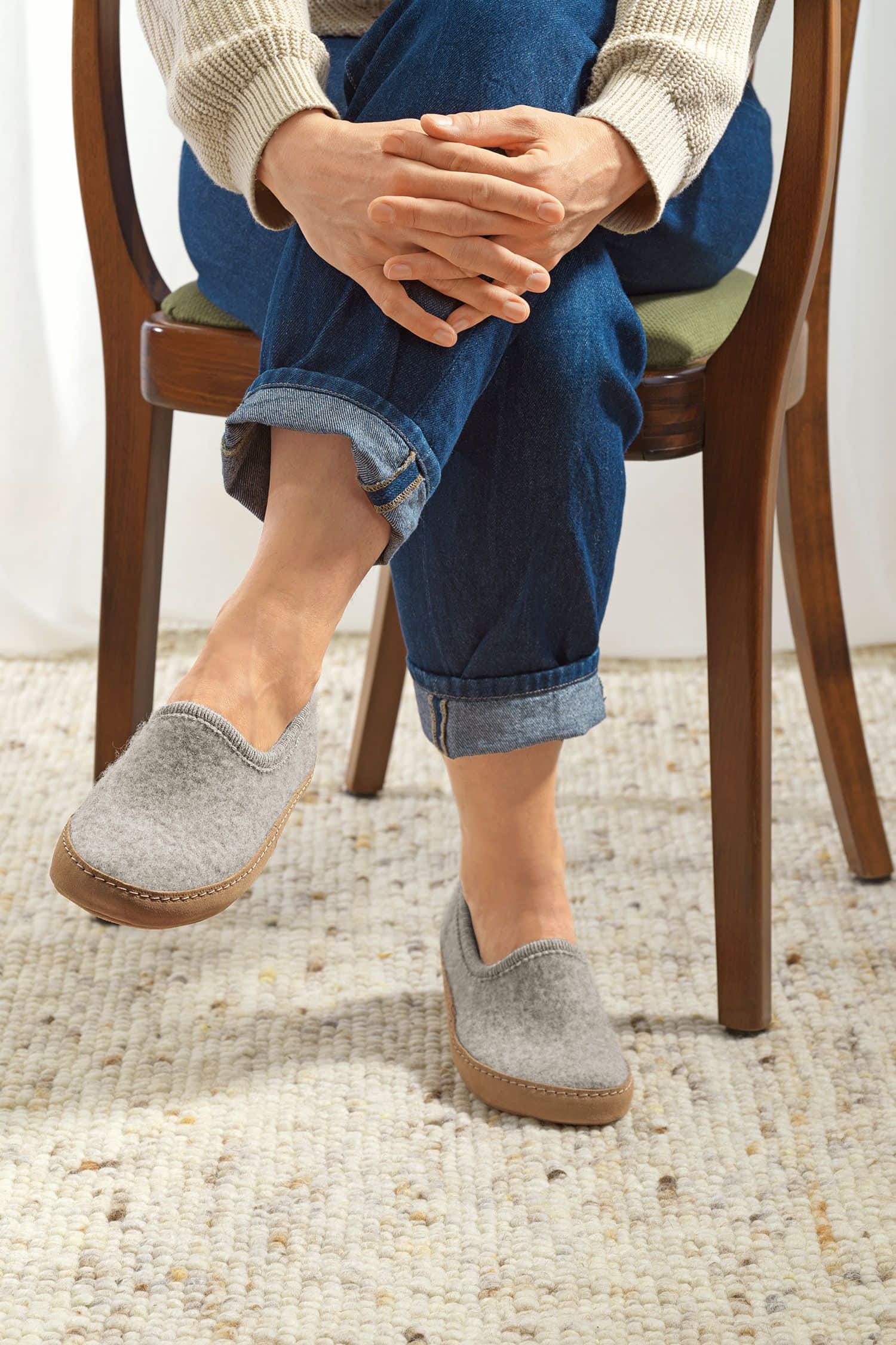 Person trägt hellgraue Finkhof Hausschuhe aus bio Wolle (kbT) mit einer Sohle aus pflanzlich gegerbtem Rindsleder