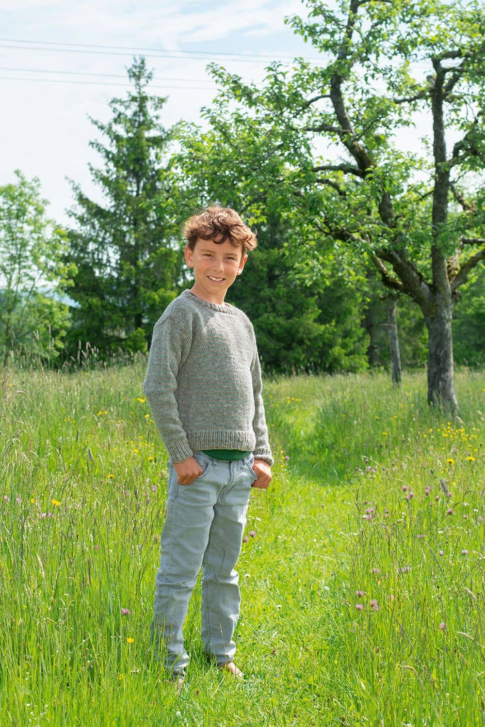 Junge mit grauem Pulli auf Wiese als Beispielprojekt für das Buch ,,Kindersachen stricken ohne Schnickschnack"
