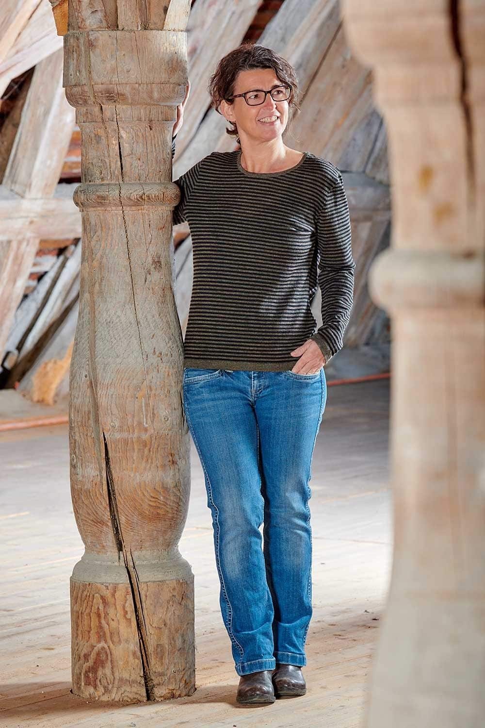 Frau lehnt an Balken und trägt ein schwarz braun gestreiftes Wollshirt aus bio Wolle (kbT) vom Finkhof