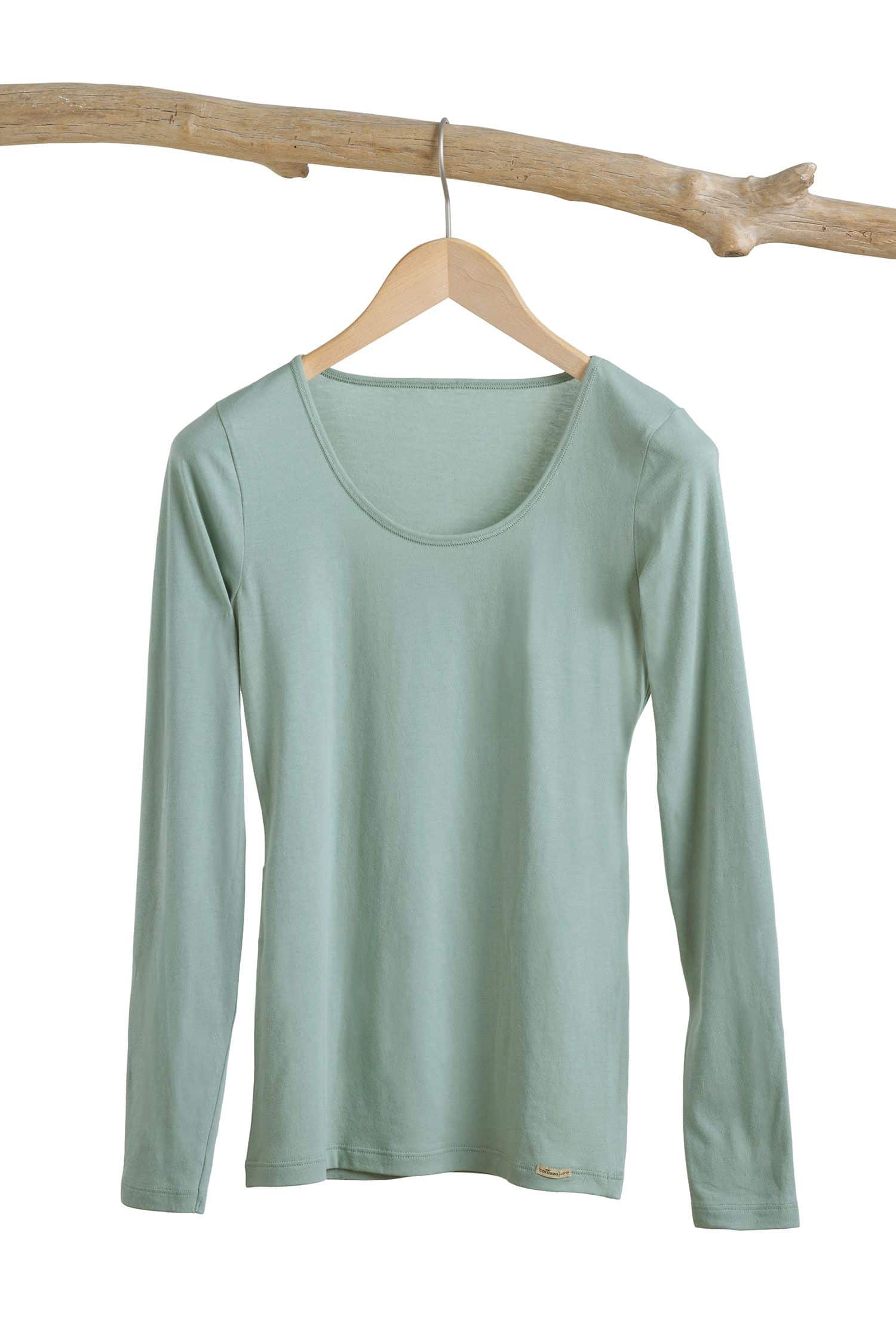 schilfgrünes Langarmshirt aus bio Baumwolle (kbA) und Elasthan hängt mit Bügel an einem Ast