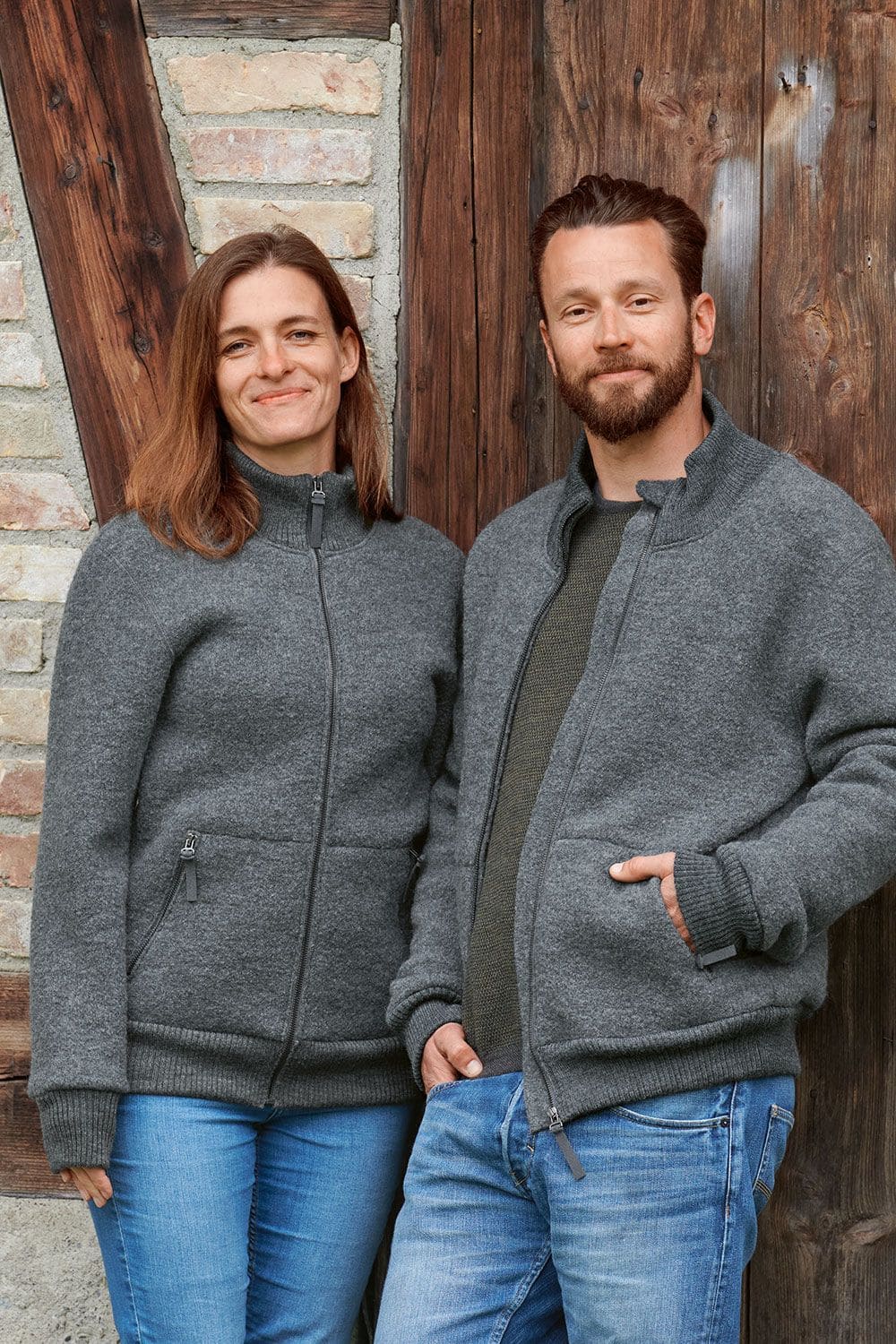 Frau und Mann vor Holztor mit grauer Finkhof Jacke Toni aus bio Wolle (kbT) mit Jeans