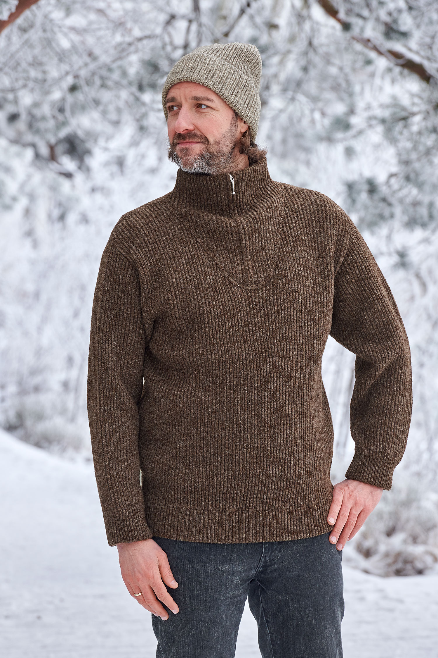 Mann in Schneelandschaft trägt einen braunen Finkhof Troyer aus bio Wolle (kbT) und eine graue Mütze