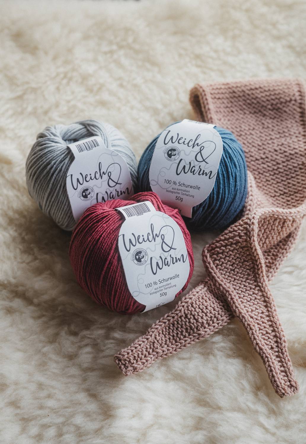 rosafarbener Mini-Schal liegt mit der Finkhof Weich&Warm Wolle auf einem weißen Fell