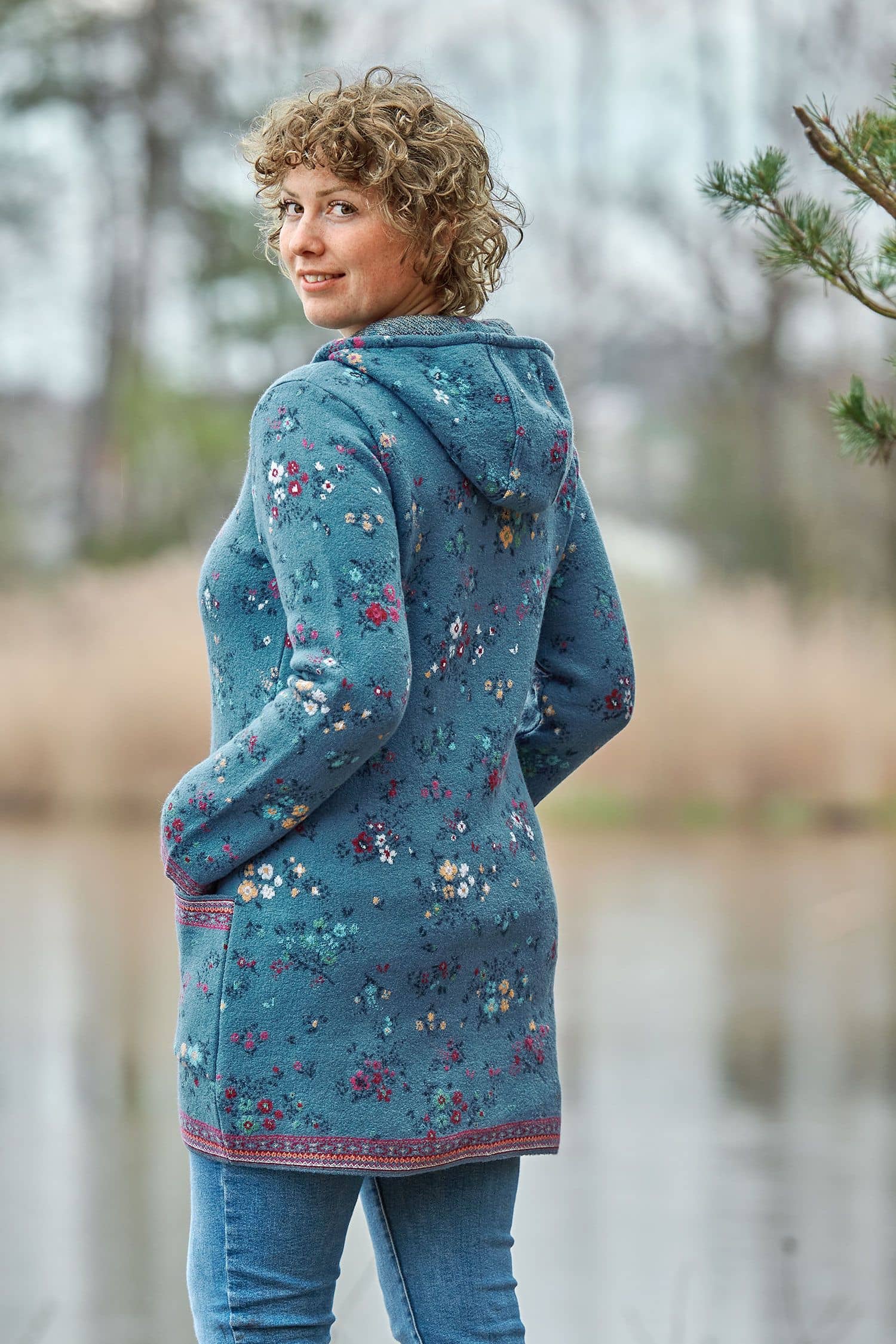 Frau von hinten mit langer blauer Kapuzenjacke aus Walkstoff mit bio Merinowolle (kbT) und Baumwolle (kbA) mit Blumenmuster
