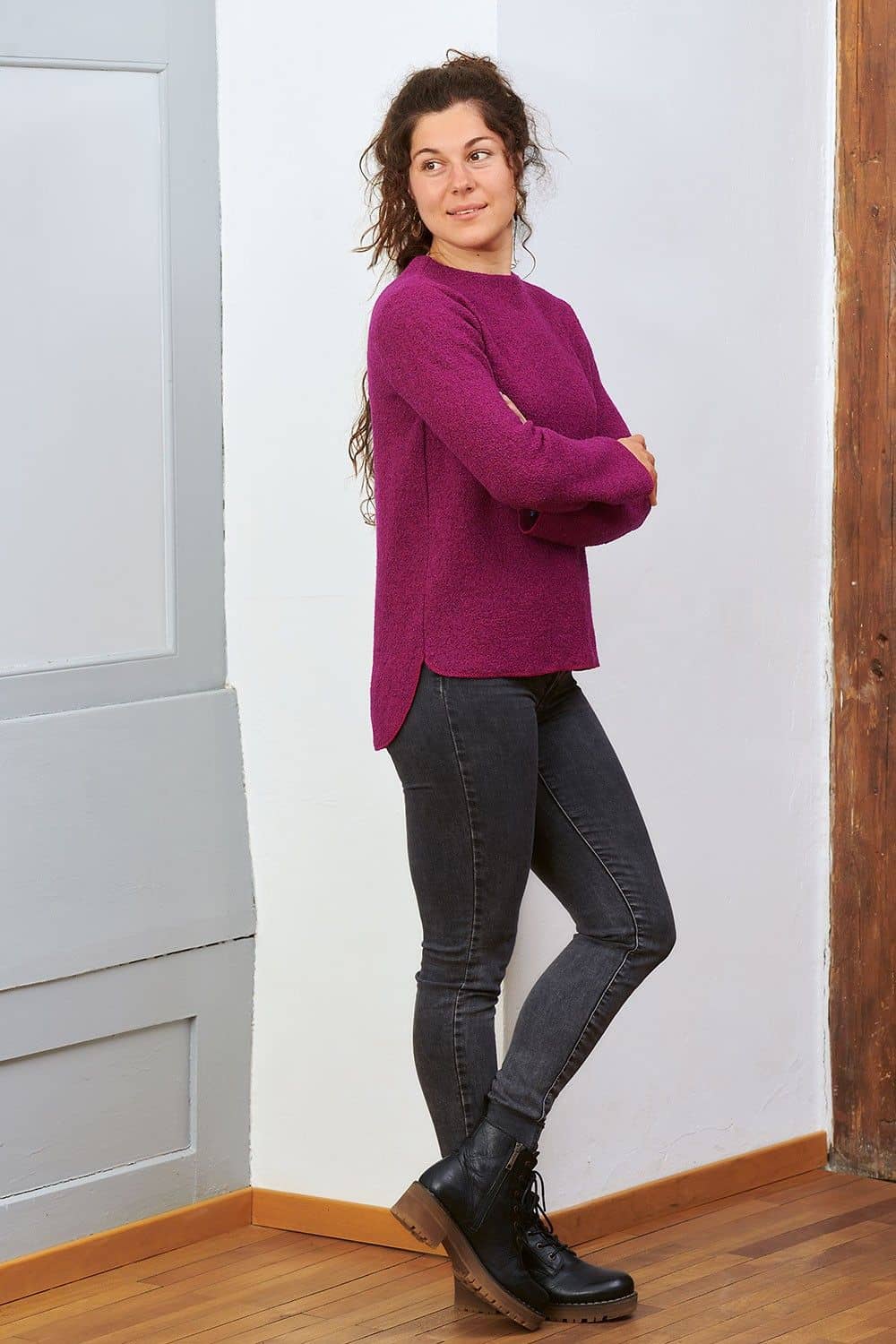 Frau mit  schwarzer Jeans steht vor weißer Wand und  trägt pinken Pulli aus bio Wolle (kbT)