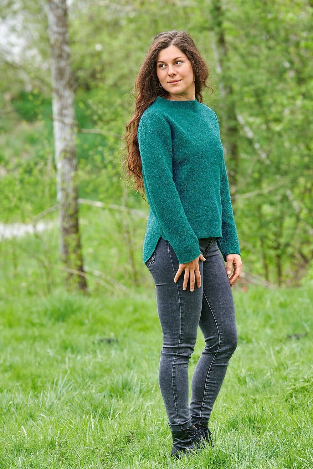 Frau steht in der Natur und trägt türkisen Pulli aus bio Wolle (kbT) und eine schwarze Jeans