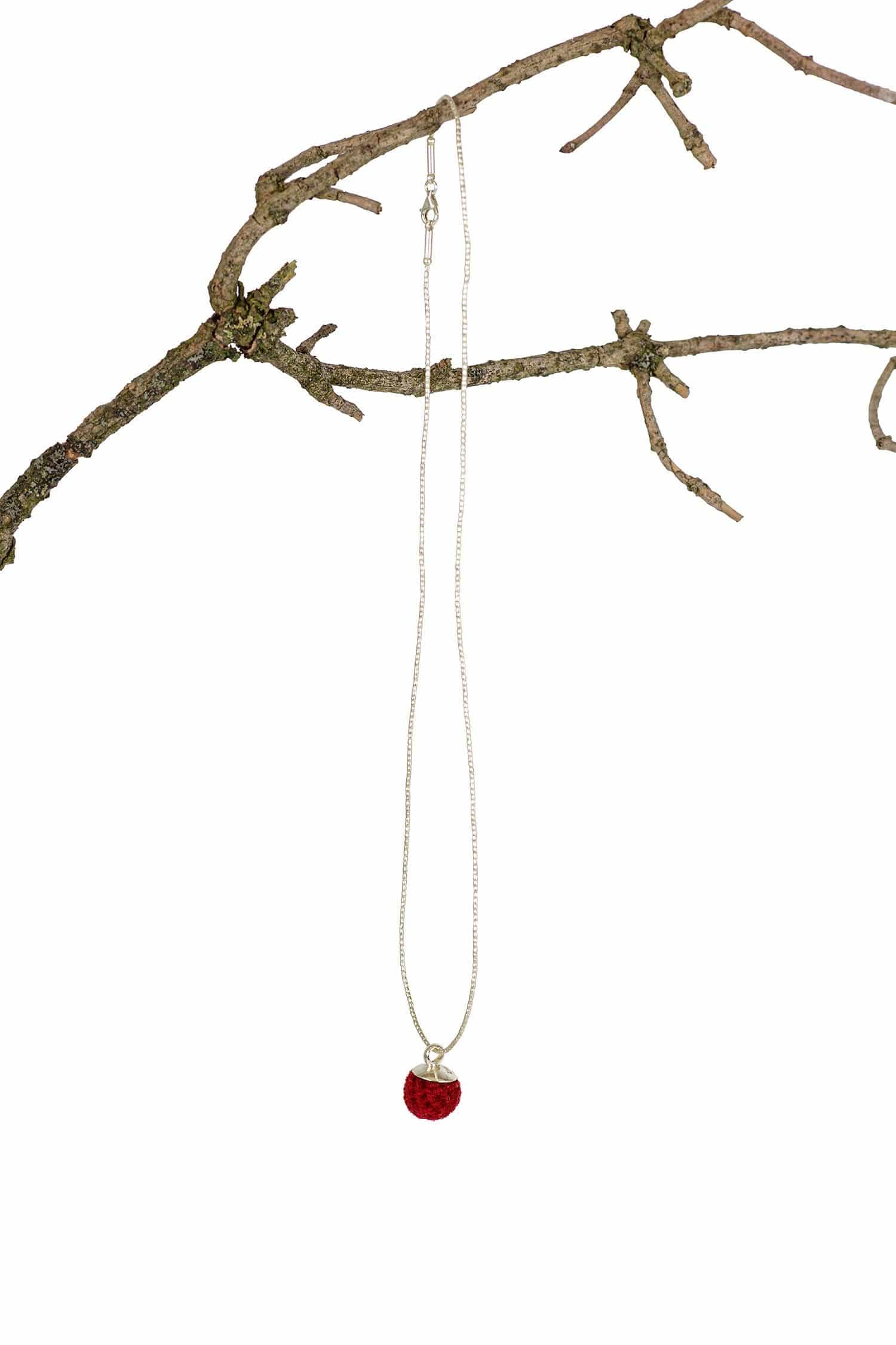 Frau trägt silberne Kette mit purpurrotem Kettenanhmger in Form einer Perle auf einen Ast gehängt
