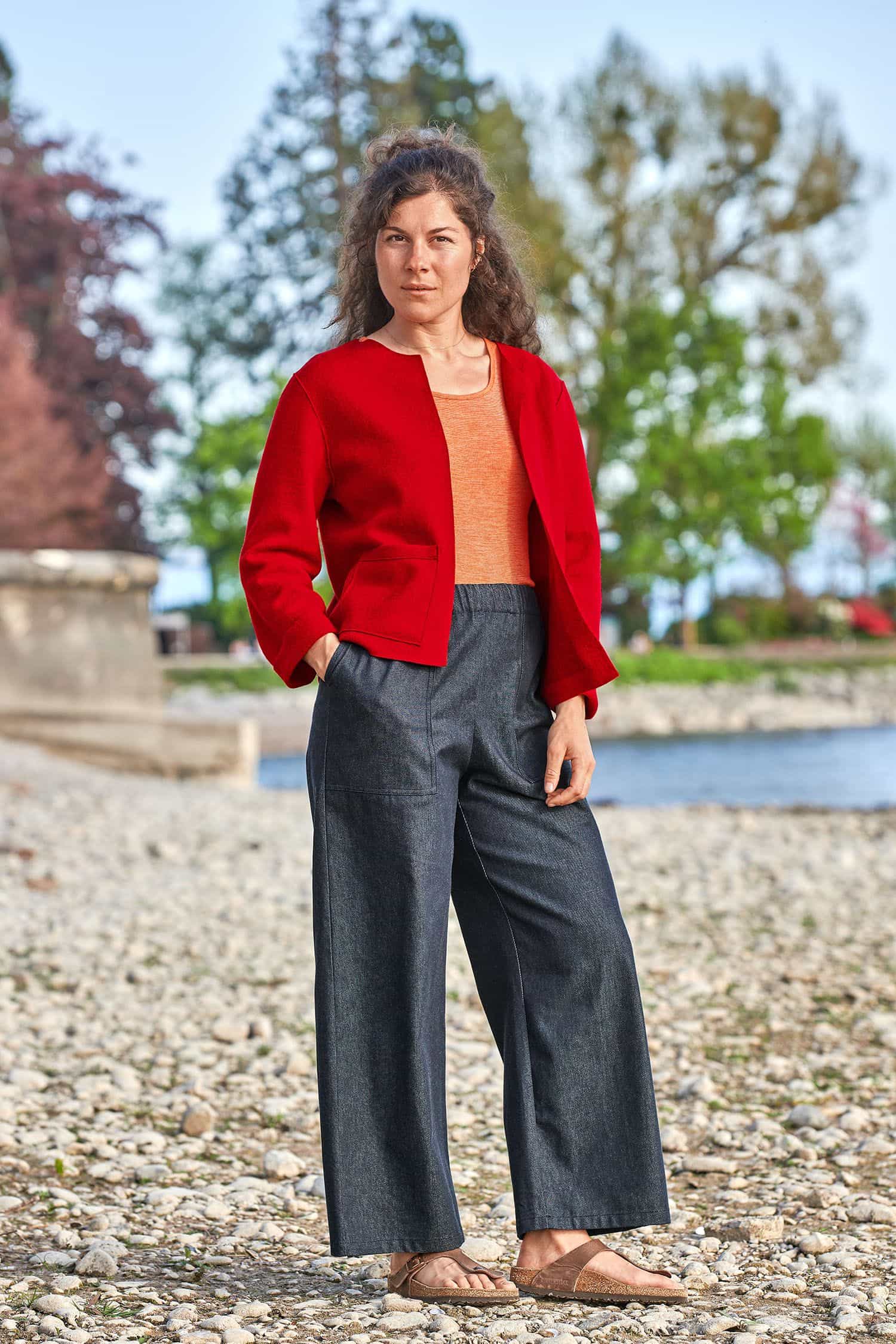 Damen-Jeanshose Frau trägt eine gerade geschnittene Jeansstoffhose aus bio Baumwolle (kbA) vom Finkhof mit orangem Shirt und roter Jacke