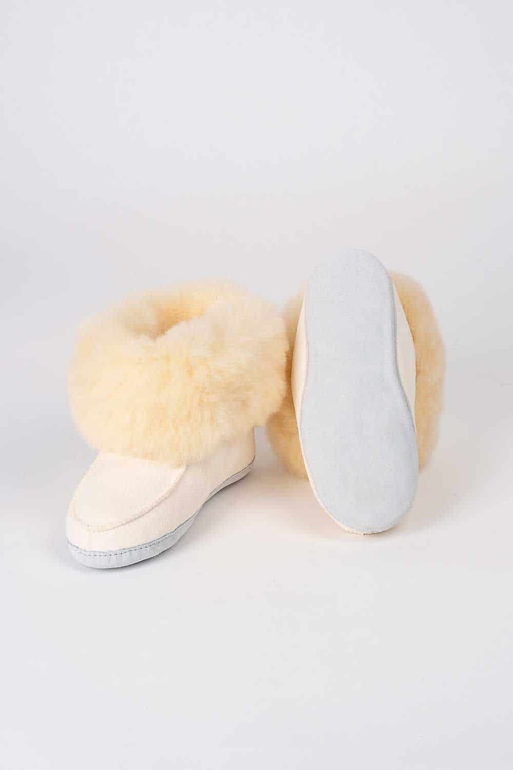 Weiße Finkhof-Fellschuhe aus Schaffell und Rindsleder, einer stehend, einer mit Sohle zur Kamera vor hellem Hintergrund