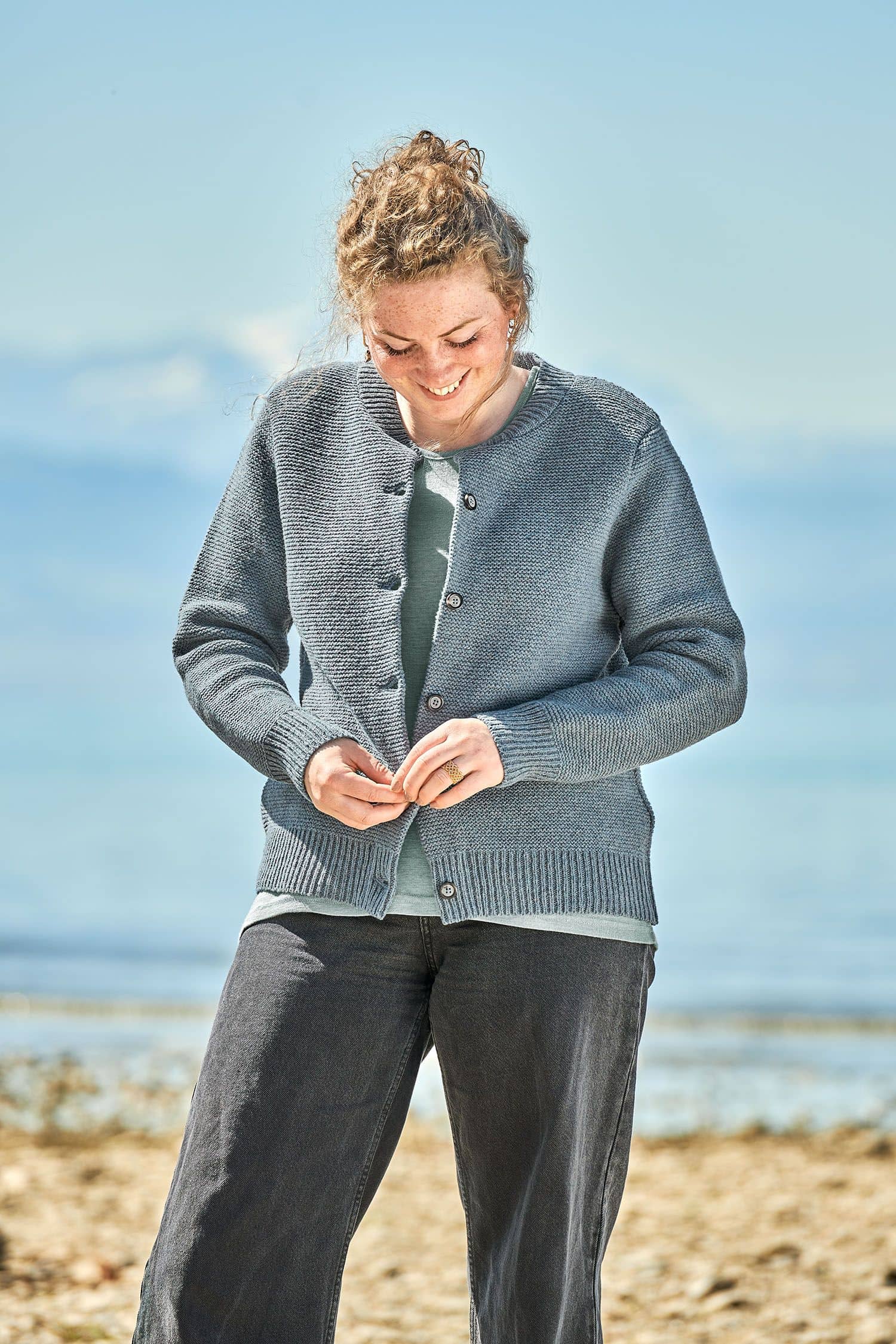 Frau trägt eine schwarze Jeans, ein türkises Shirt und eine rauchblaue Strickjacke vom Finkhof aus bio Merinowolle (kbT)