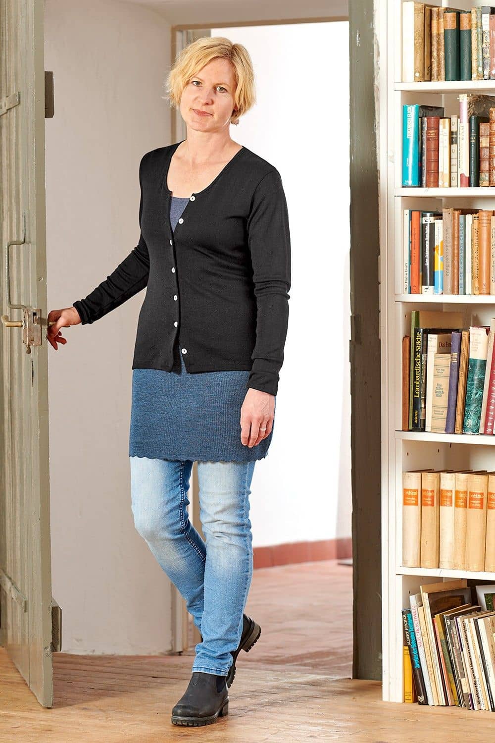 Kurzrock jeans Gr. S Frau kommt mit schwarzem Cardigan und blauem Finkhof Kurzrock aus bio Wolle (kbT) durch eine Tür