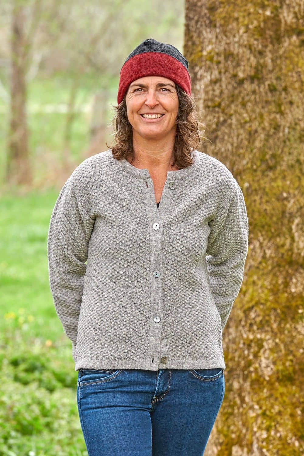 Frau mit grauer Strickjacke trägt eine rot graue Wendemütze aus bio Wolle (kbT) vom Finkhof