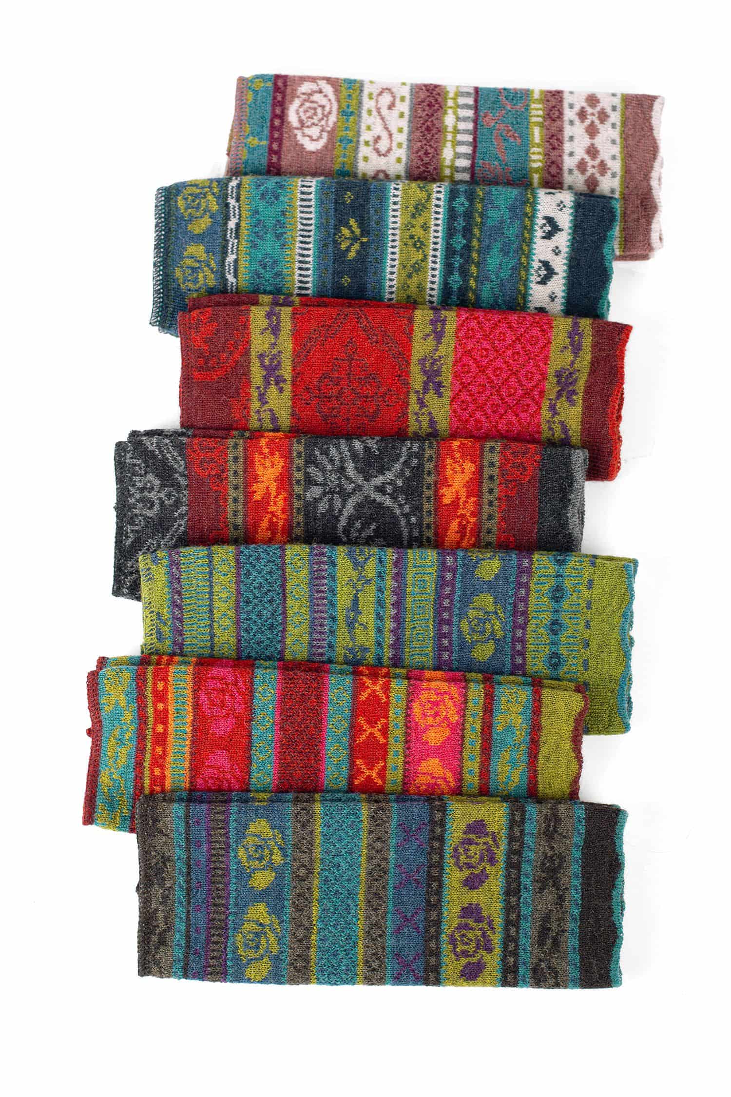 Gemusterte Armstulpen gemusterte Armstulpen aus bio Wolle (kbT) liegen in sieben Farben versetzt aufeinander auf weiß