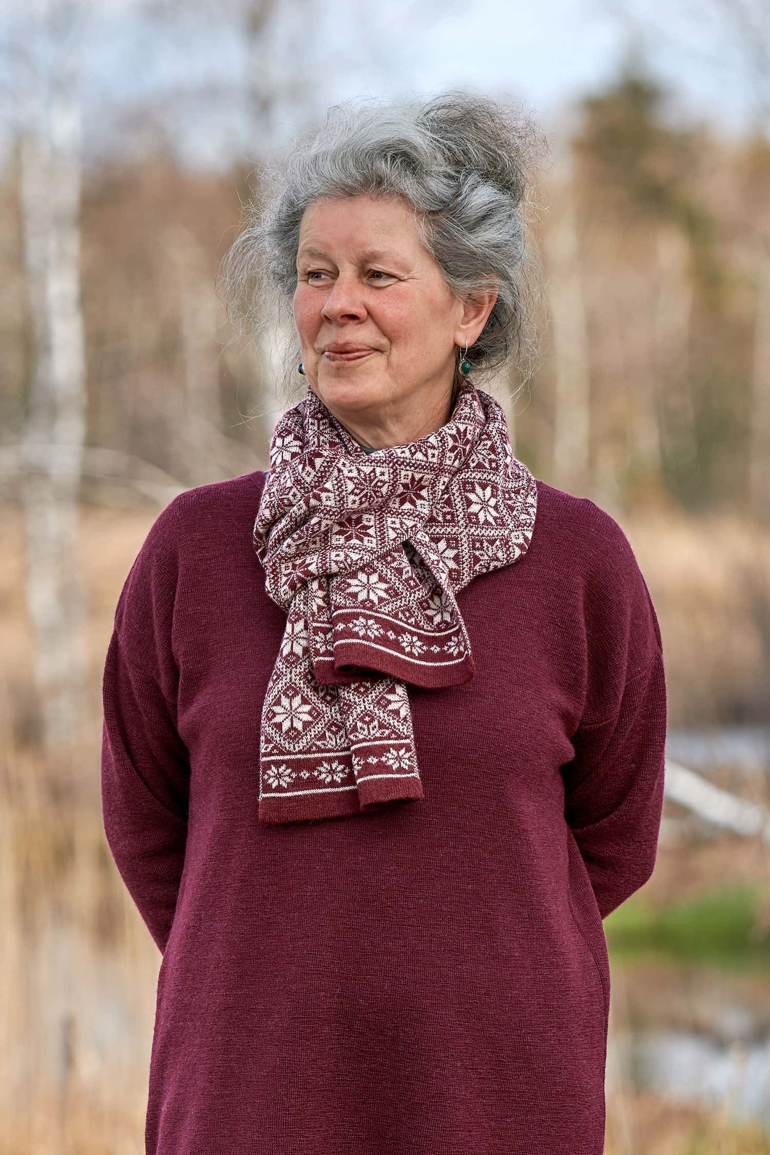 Frau mit weinrotem Kleid trägt burgunderroten Schal mit Norwegermuster aus bio Wolle (kbT)