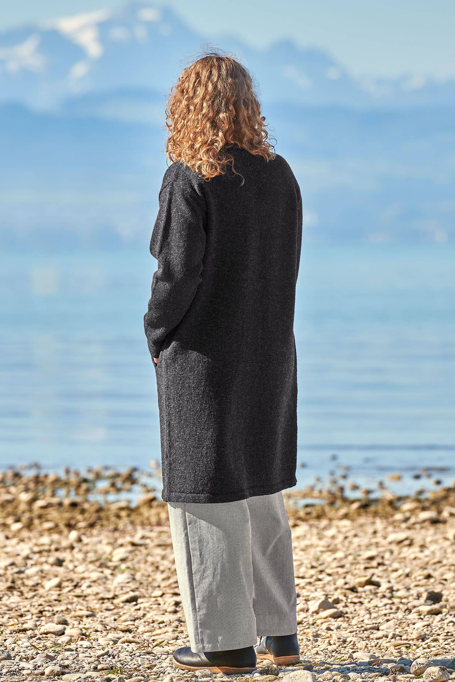 Rückansicht von Frau mit dunkelgrauem Finkhof Strickmantel aus bio Wolle (kbT) und weiter Hose