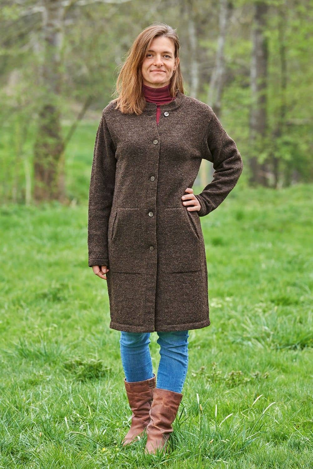 Finkhof-Strickmantel braun Gr. M Frau steht mit braunen Stiefeln und braunem Finkhof Strickmantel aus bio Wolle (kbT) auf einer Wiese