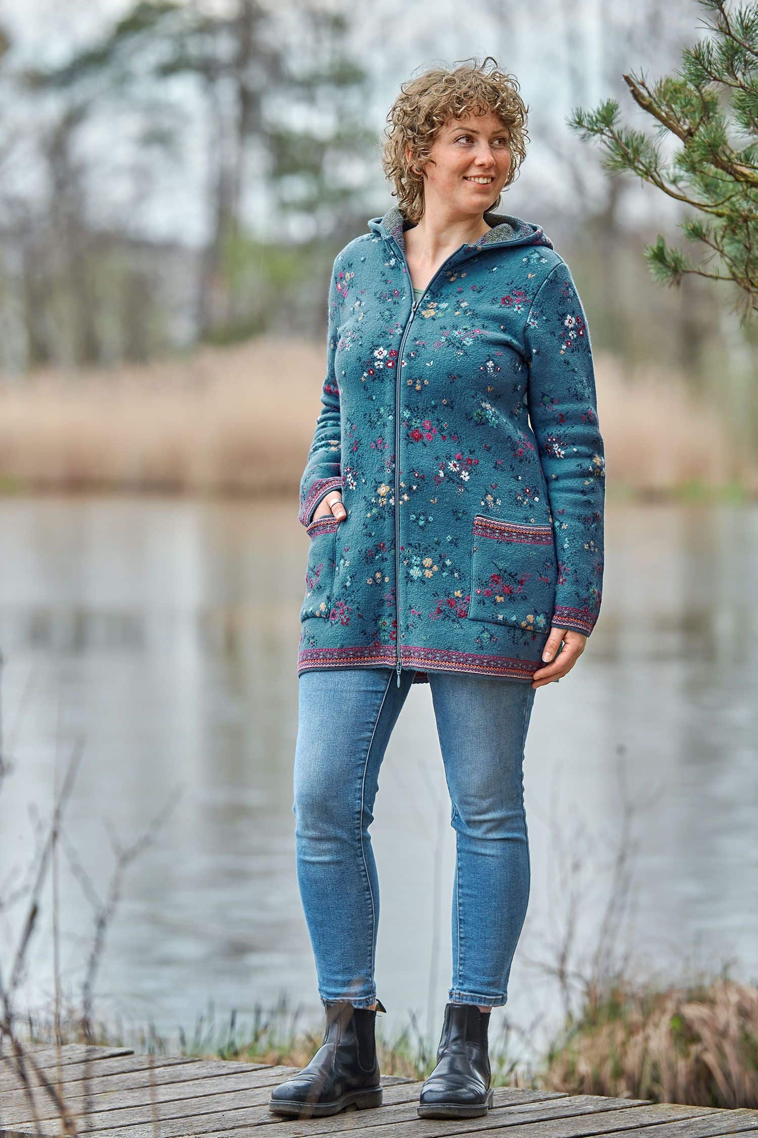 Frau auf Steg trägt lange blaue Kapuzenjacke aus Walkstoff mit bio Merinowolle (kbT) und Baumwolle (kbA) mit Blumenmuster