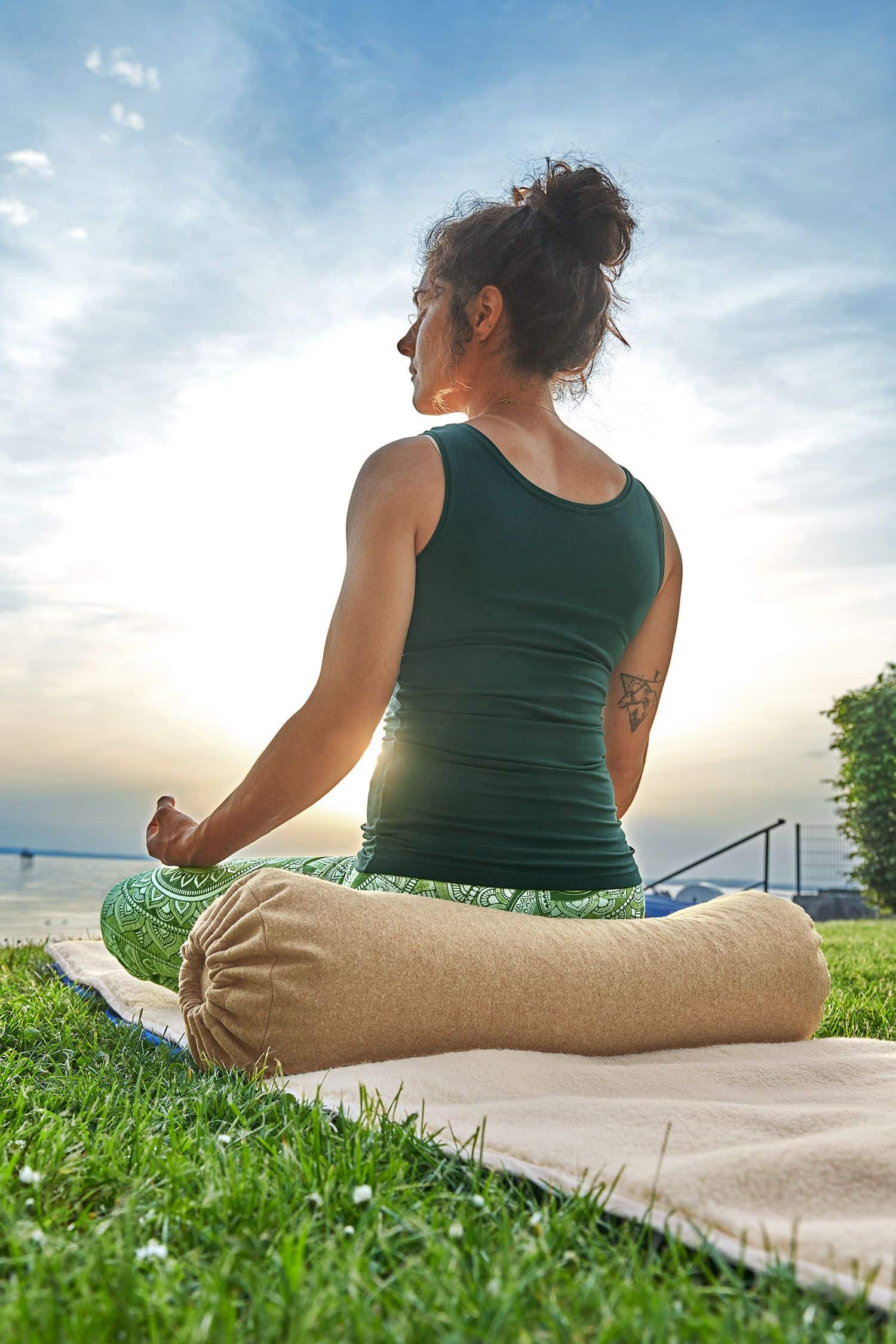 Rückansicht von Frau in grüner Yoga Kleidung auf heller Meditationsrolle aus Loden mit Dinkelspelz gefüllt vom Finkhof