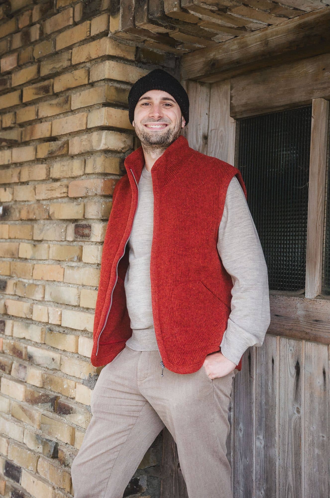Mann trägt braunes Wollshirt, eine Mütze und eine rote Wollwalkweste aus bio Wolle (kbT) vom Finkhof