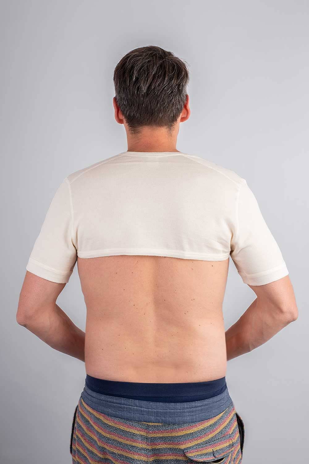 Rückansicht von einem Mann mit gestreifter Hose und einem weißen Schulterwärmer aus bio Wolle (kbT) und Seide