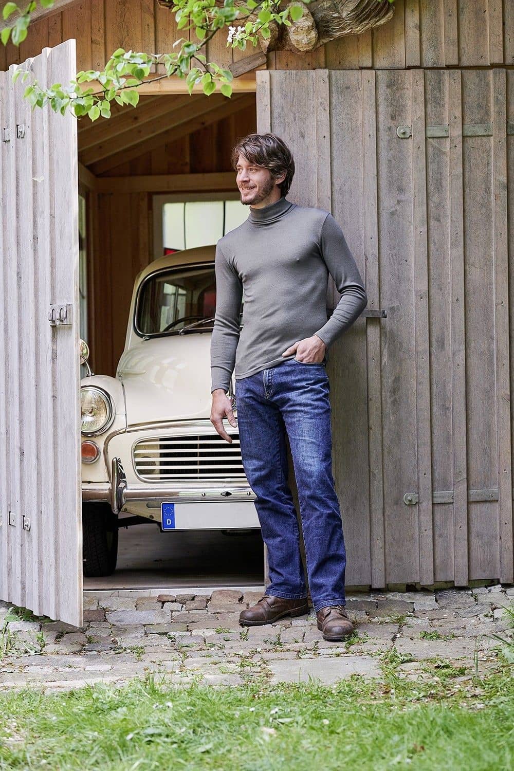 Mann steht vor Holztor und trägt graues Shirt mit Rollkragen aus bio Baumwolle (kbA) und Seide