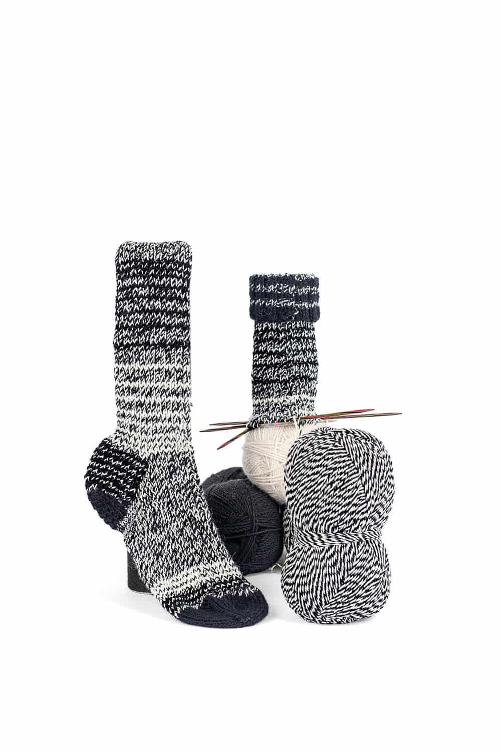 feine Finkhof Sockenwolle mit Melangeeffekt aus bio Wolle (kbT) in naturweiß/ schwarz mit Wollknäulen und Stricksocken