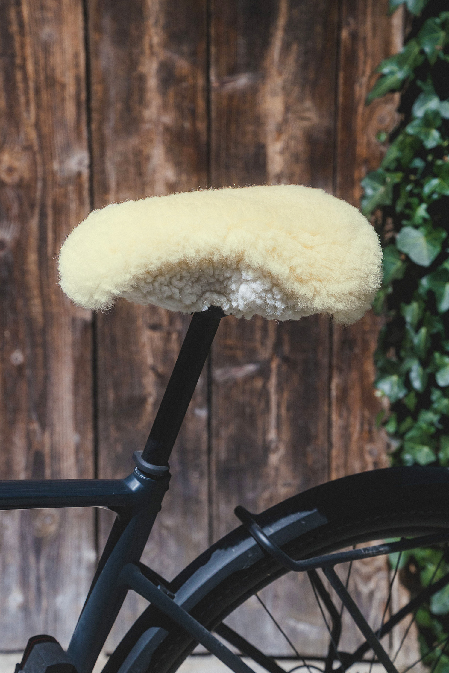 relugan gegerbter breiter Finkhof Sattelbezug aus bio Wolle (kbT) und Schaffell auf Fahrrad mit Steinwand im Hintergrund