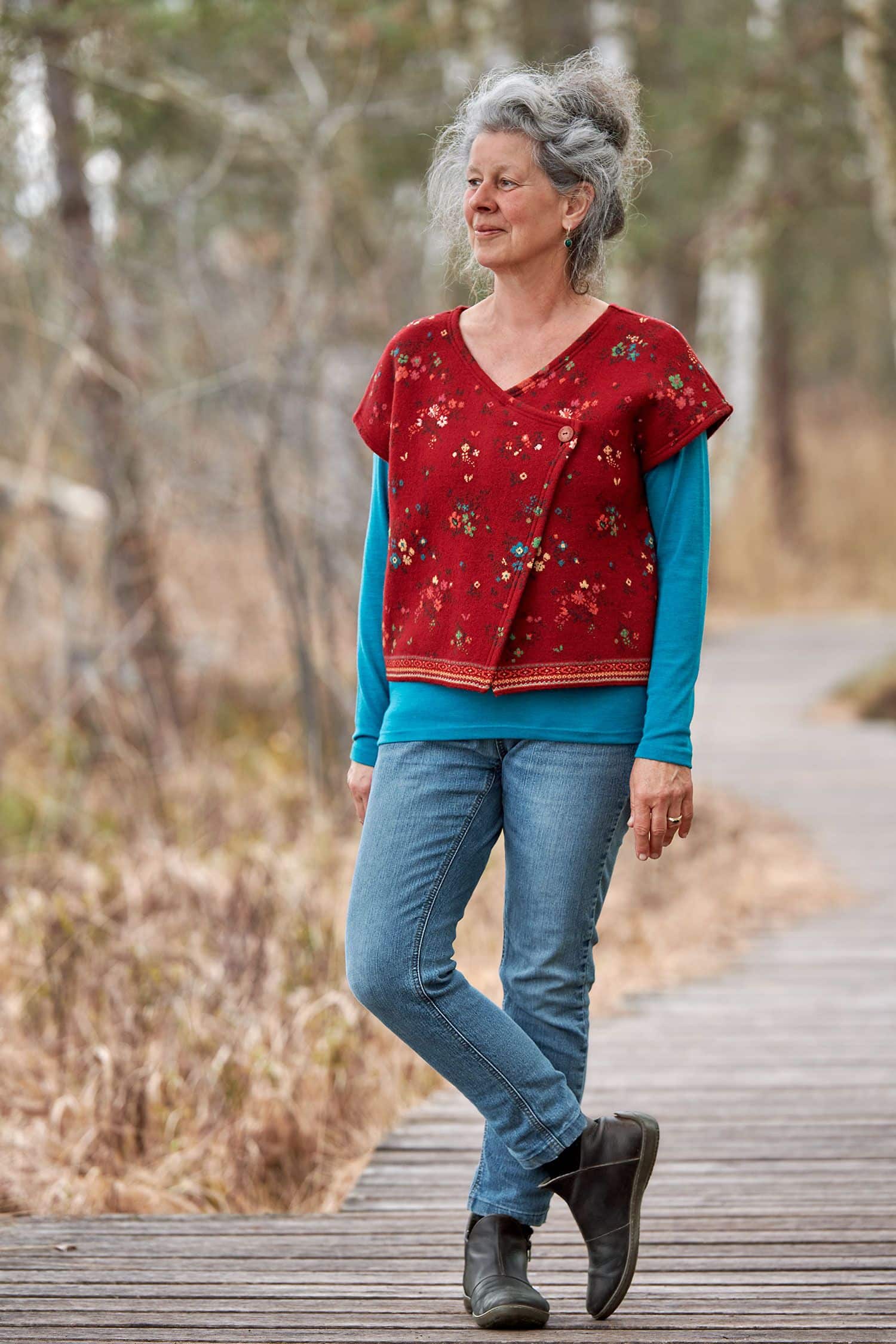 Frau mit türkisem Shirt trägt eine rot gemusterte Weste ohne Ärmel aus bio Merinowolle (kbT) und bio Baumwolle (kbA)