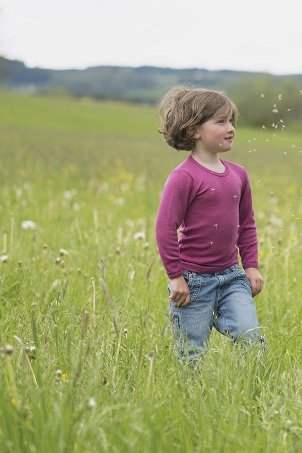 Kind trägt fuchsiafarbenes Wolle Seide Langarmshirt aus bio Wolle (kbT) und spielt dabei auf Wiese