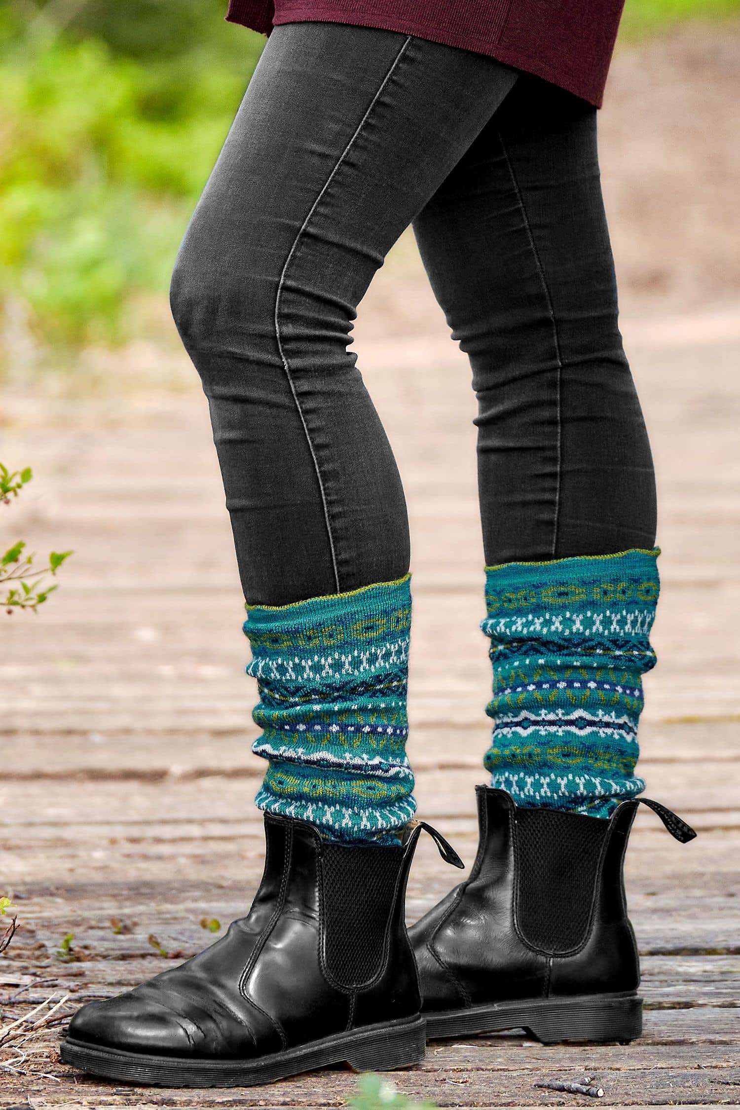 Person trägt schwarze Stiefel, Jeans und türkise Beinstulpen mit nordischem Muster aus bio Wolle (kbT)