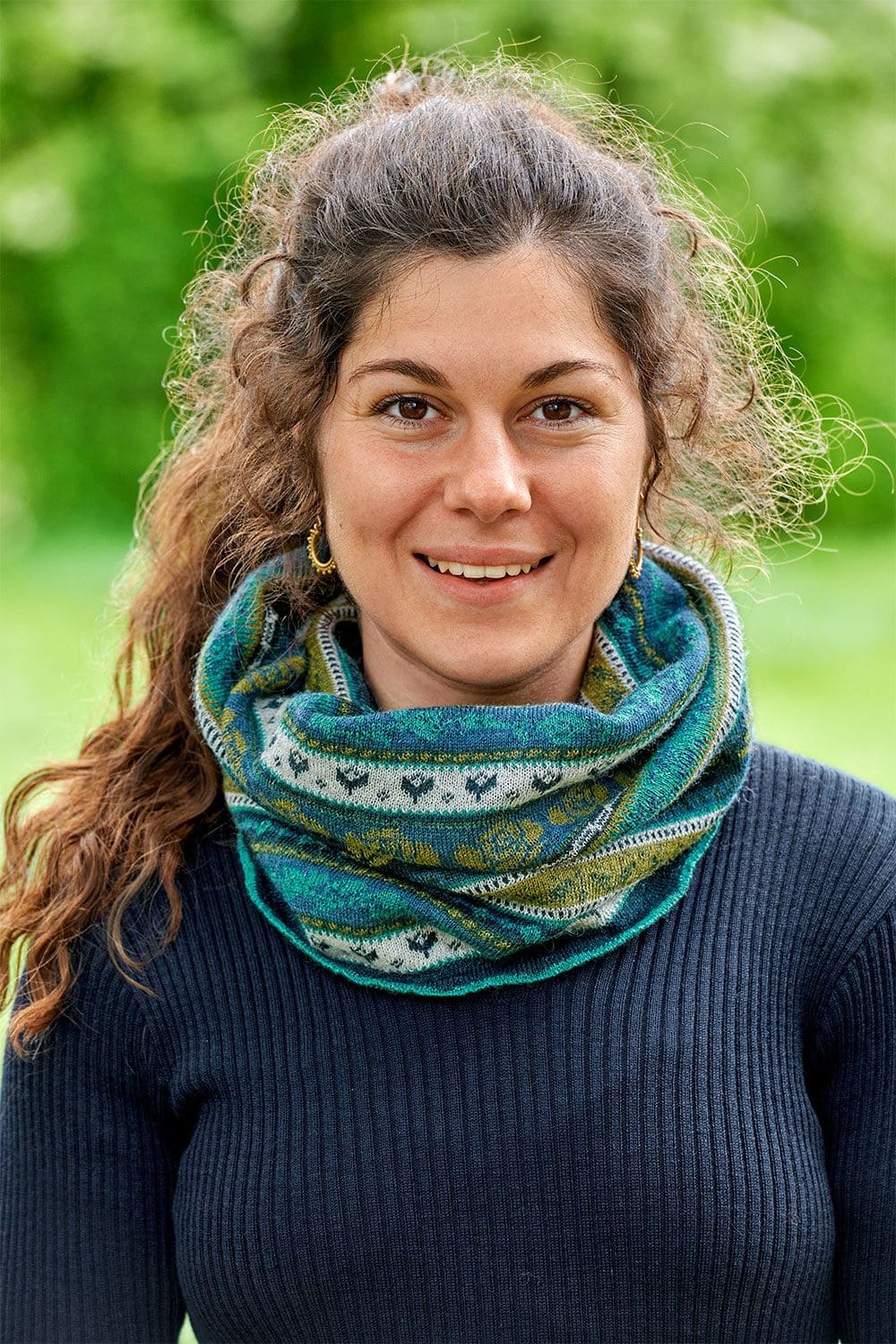 Frau mit Rippshirt und dunklen Locken trägt blau grün gemusterten Loopschal aus bio Wolle (kbT)