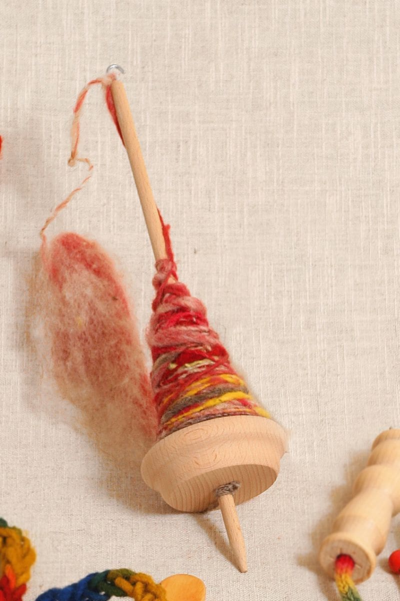 Handspindel Handspindel aus Holz mit etwas rotmelierter Wolle liegt auf beigem Untergrund