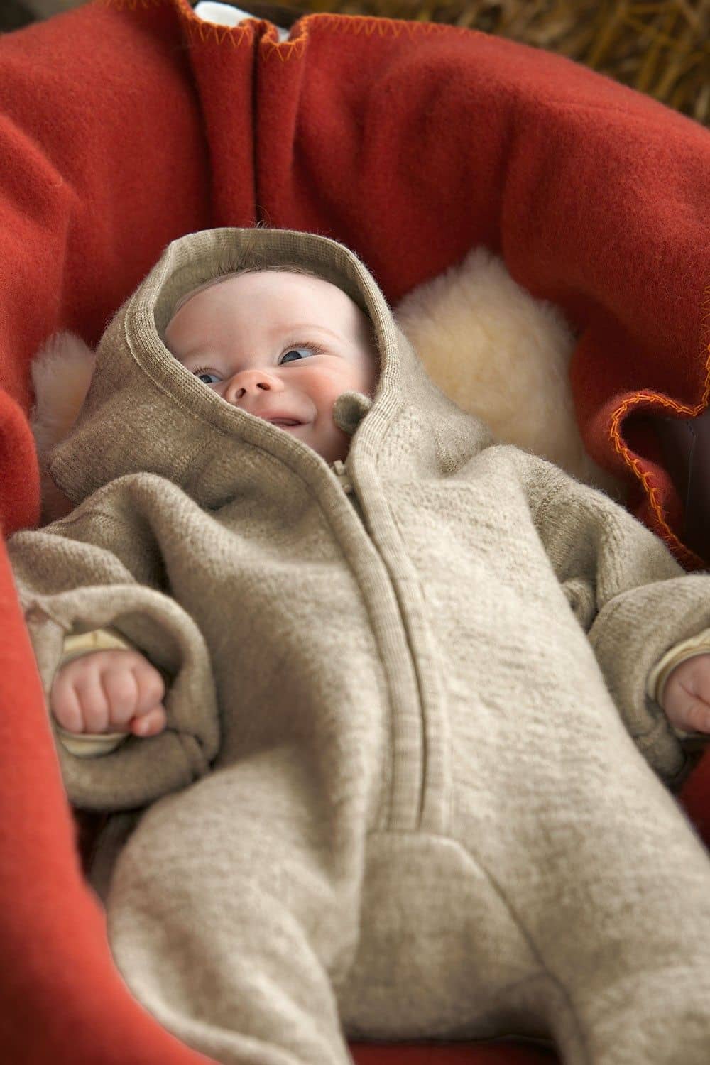 Kind liegt auf einer roten Decke und trägt einen naturmelierten Walkoverall aus bio Wolle (kbT) vom Finkhof