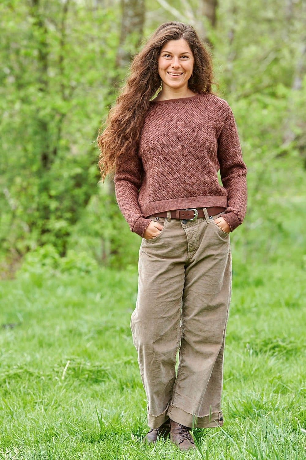 Frau läuft auf Wiese mit altrosa Pullover aus bio Wolle (kbT) und brauner Hose