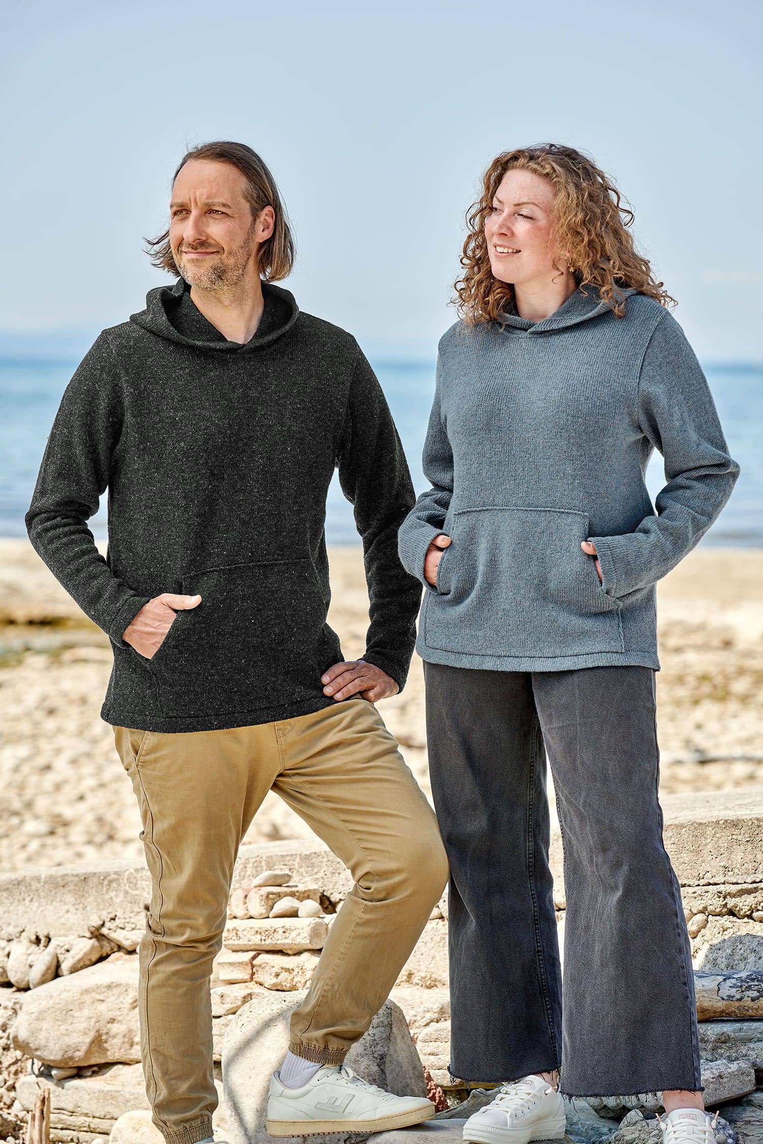 Finkhof-Kapuzenpulli Mann und Frau stehen auf Steinen und tragen Kapuzenpullover vom Finkhof aus bio Wolle (kbT)