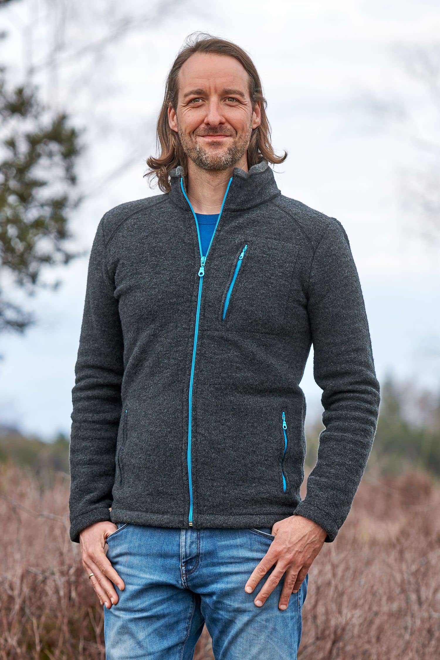 Mann trägt dunkelgraue Wollfleecejacke mit türkisen Reißverschlüssen aus bio Wolle (kbT)