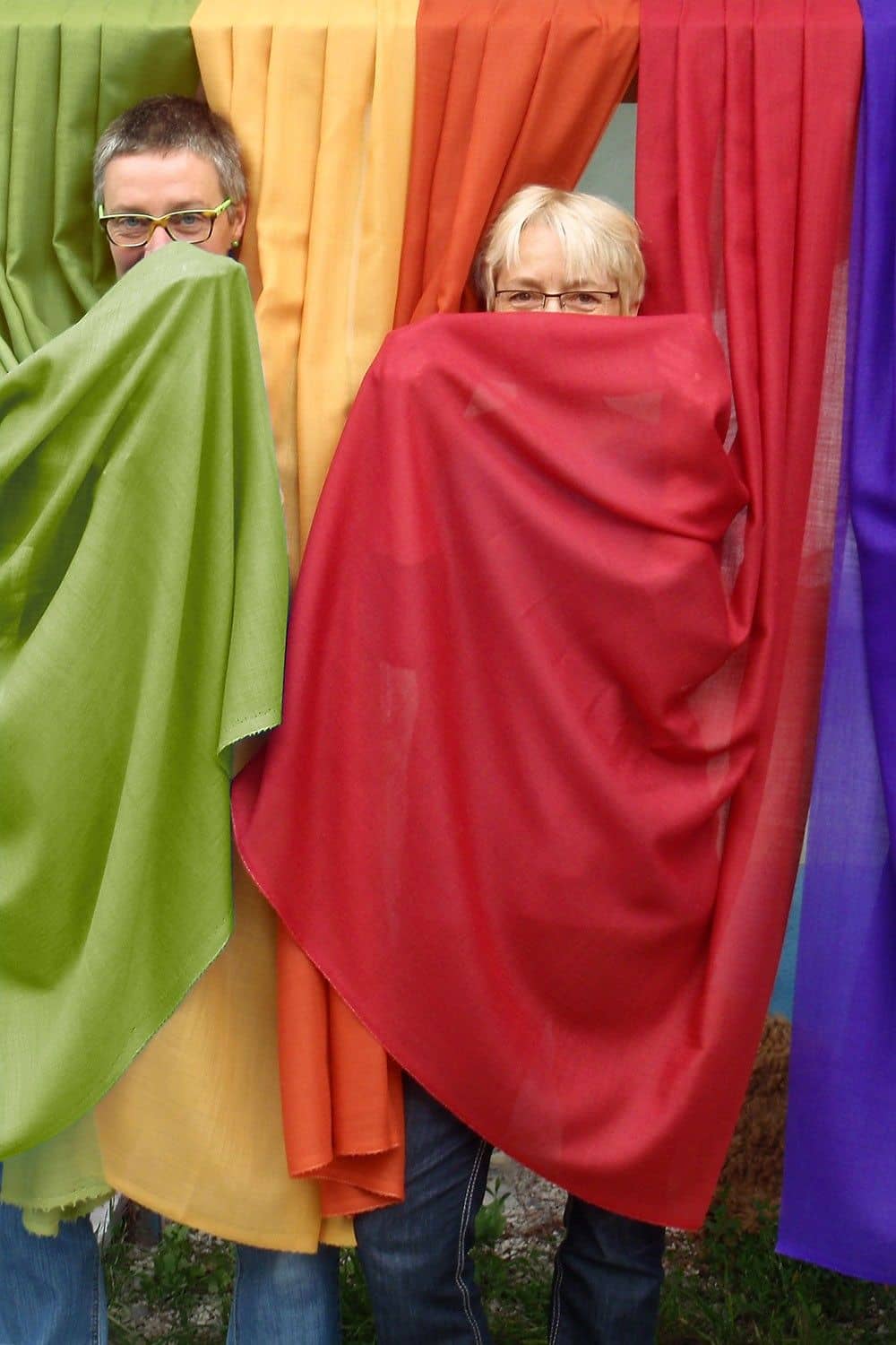 Frauen stehen hinter Wollmouselinestoffbahnen und verdecken damit ihre Gesichter