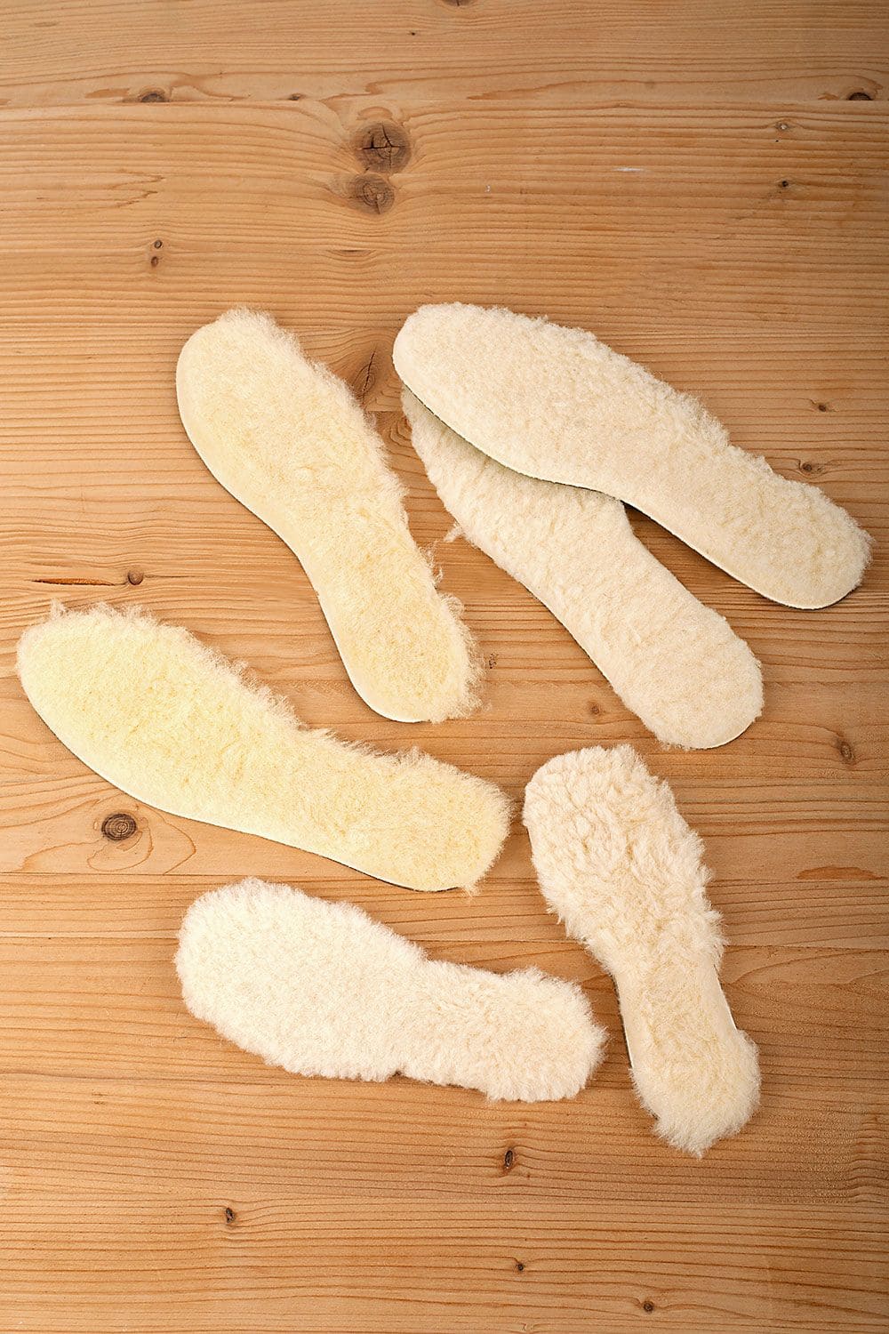 helle flauschige relugan gegerbte Fellsohlen vom Finkhof in verschiedenen Größen auf braunem Holzboden ausgelegt