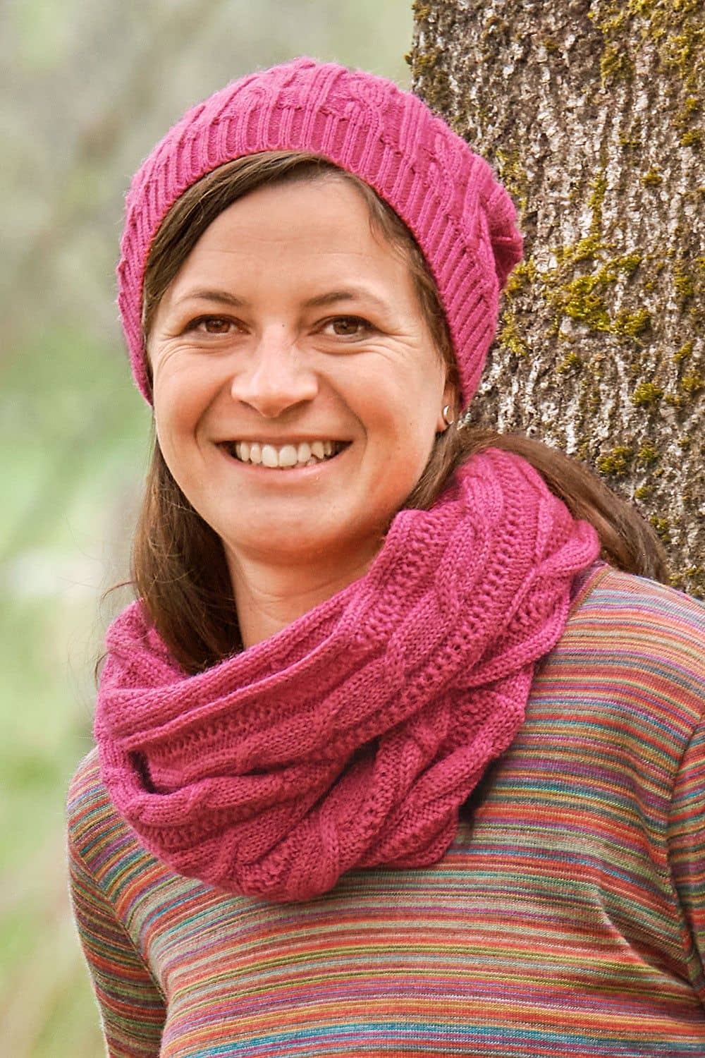 Frau mit buntmeliertem Shirt trägt eine pinke Ballonmütze und einen Schal aus bio Merinwolle (kbT) vom Finkhof