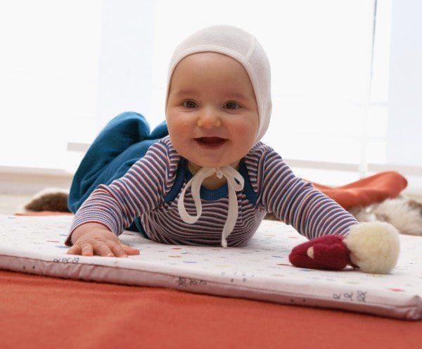 baby-muetze-wolle5cee3bdfd4bf0 Baby mit Streifenshirt und weißer Babymütze liegt auf de Bauch und lacht