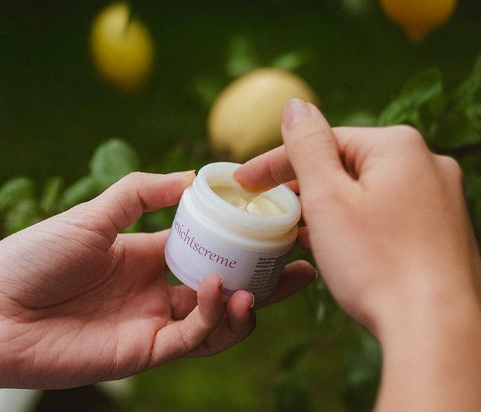 Person hat geöffnete Finkhof Gesichtscreme in der Hand und taucht einen Finger ein