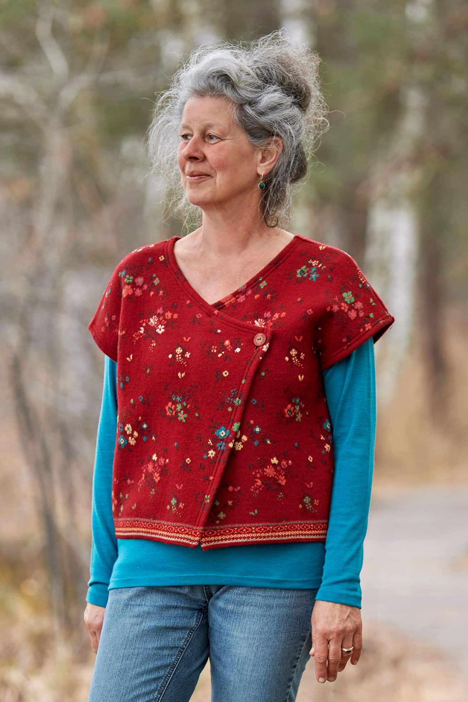 Frau mit türkisem Shirt trägt eine rot gemusterte Weste ohne Ärmel aus bio Merinowolle (kbT) und bio Baumwolle (kbA)