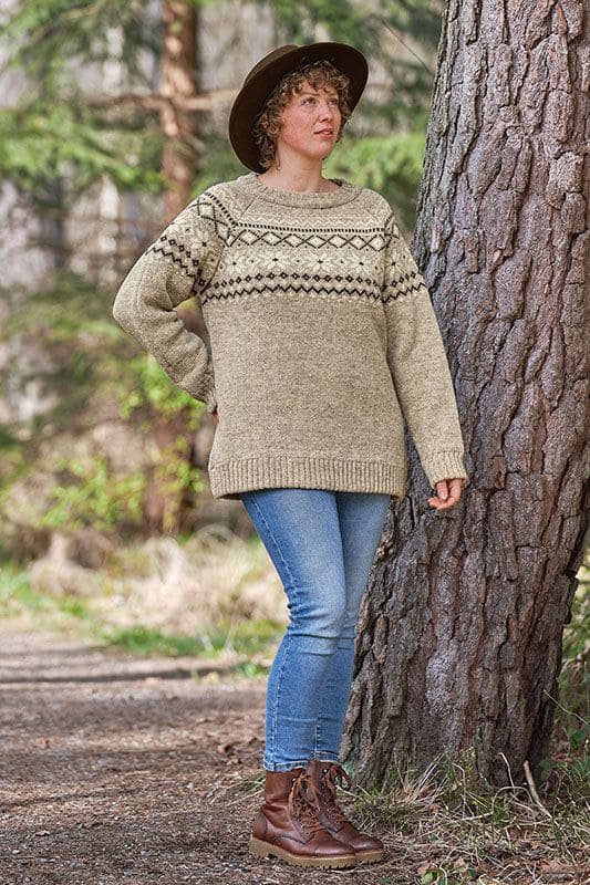 Frau mit Hut und Jeans steht neben Baum und trägt grauen Finkhof Norwegerpulli aus bio Wolle (kbT)