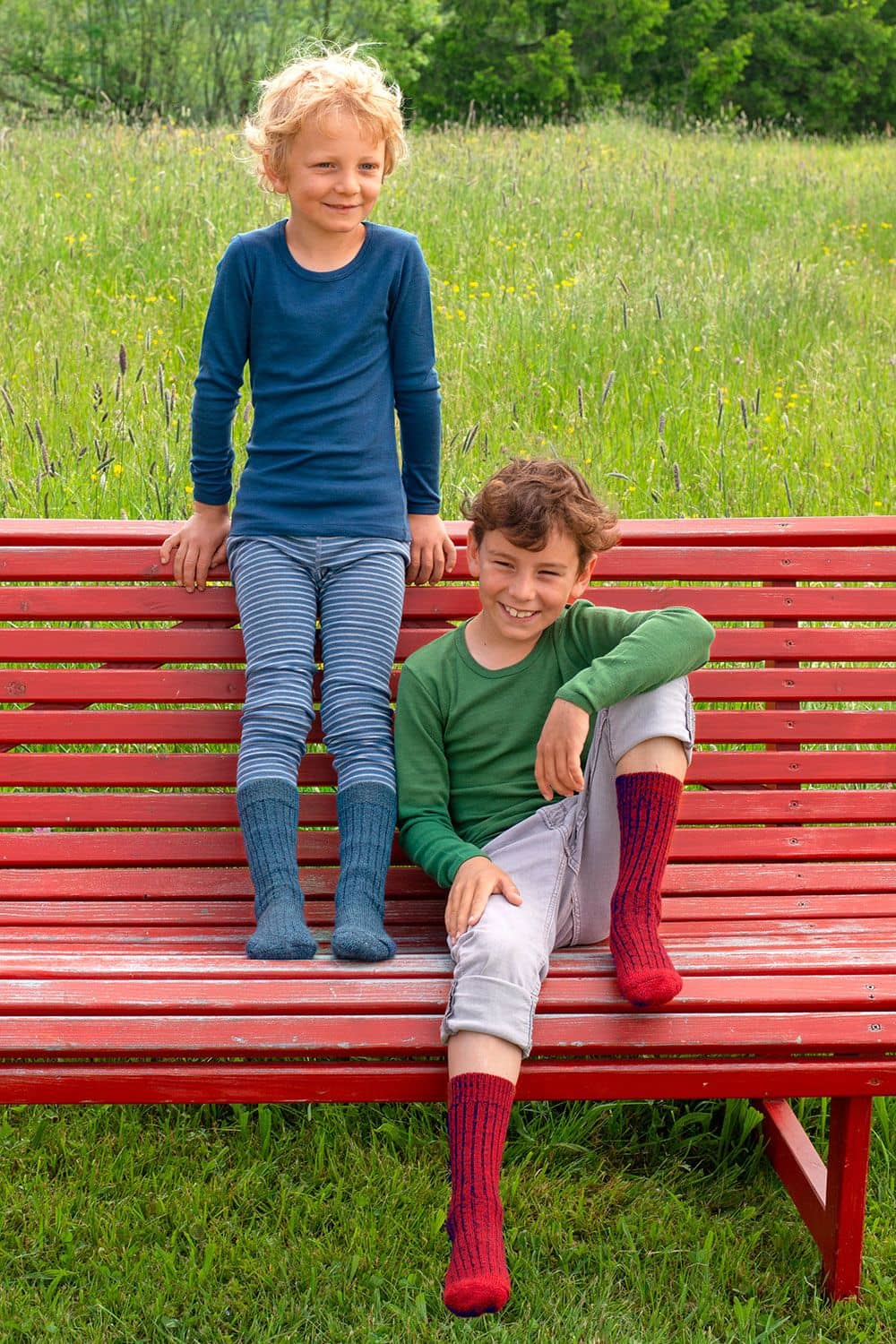 Wollplüschsocken Jungs sitzen mit blauen und roten Wollplüschsocken aus bio Wolle (kbT) auf roter Bank